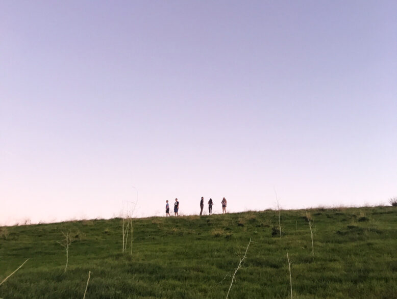 purple sky over people on a hill in the distance.