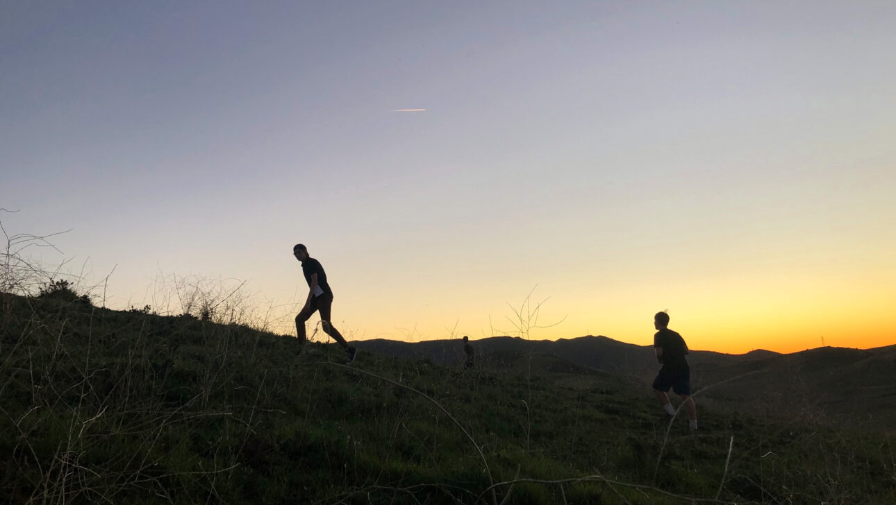 teens climbing up a hill in front of a sunset.